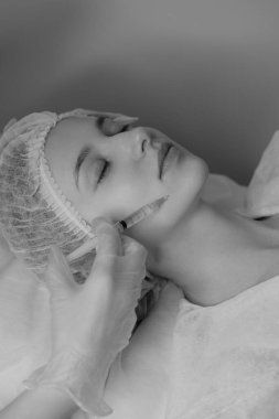 Açık tenli bir kadının estetik ameliyat sırasında botoks yaptırdığı siyah beyaz bir fotoğraf. Klinik ortamda estetik tıp ve güzellik tedavisi. Yüksek kalite fotoğraf