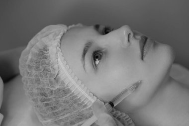 Açık tenli bir kadının estetik ameliyat sırasında botoks yaptırdığı siyah beyaz bir fotoğraf. Klinik ortamda estetik tıp ve güzellik tedavisi. Yüksek kalite fotoğraf