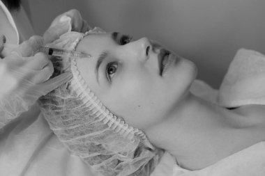 Açık tenli bir kadının estetik ameliyat sırasında botoks yaptırdığı siyah beyaz bir fotoğraf. Klinik ortamda estetik tıp ve güzellik tedavisi. Yüksek kalite fotoğraf