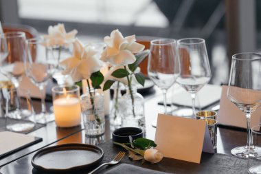 Lüks siyah bir masada sofistike bir kutlama için şık bir masa. Altın şamdanlar, şarap kadehleri, beyaz güller, peçeteler ve bir kağıt isim kartı... İnce bir atmosfer yaratır..