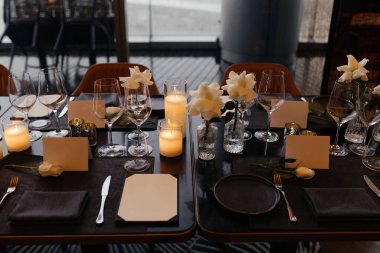 Lüks siyah bir masada sofistike bir kutlama için şık bir masa. Altın şamdanlar, şarap bardakları, beyaz güller, peçeteler ve bir kağıt isim kartı daha rafine bir ortam yaratır. Yüksek kalite fotoğraf