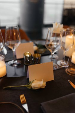 Lüks siyah bir masada sofistike bir kutlama için şık bir masa. Altın şamdanlar, şarap bardakları, beyaz güller, peçeteler ve bir kağıt isim kartı daha rafine bir ortam yaratır. Yüksek kalite fotoğraf