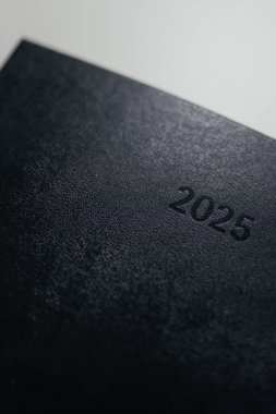 Minimalist siyah planlayıcı ya da kapağında 2025 kabartmalı metin olan bir defter. Temiz, modern tasarım. Planlama, organizasyon, zaman yönetimi kavramı. Yüksek kalite fotoğraf