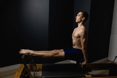 Zayıf erkek balerin pilates ekipmanlarıyla antrenman yapıyor. Zarif duruş, çekirdek gücü, vücut kontrolü. Yüksek kalite fotoğraf