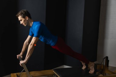 Zayıf erkek balerin pilates ekipmanlarıyla antrenman yapıyor. Zarif duruş, çekirdek gücü, vücut kontrolü. Yüksek kalite fotoğraf