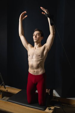 Zayıf erkek balerin pilates ekipmanlarıyla antrenman yapıyor. Zarif duruş, çekirdek gücü, vücut kontrolü. Yüksek kalite fotoğraf