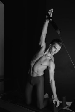 Zayıf erkek balerin pilates ekipmanlarıyla antrenman yapıyor. Zarif duruş, çekirdek gücü, vücut kontrolü. Yüksek kalite fotoğraf