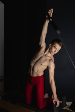 Zayıf erkek balerin pilates ekipmanlarıyla antrenman yapıyor. Zarif duruş, çekirdek gücü, vücut kontrolü. Yüksek kalite fotoğraf
