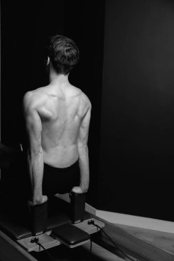 Zayıf erkek balerin pilates ekipmanlarıyla antrenman yapıyor. Zarif duruş, çekirdek gücü, vücut kontrolü. Yüksek kalite fotoğraf