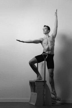 Zayıf erkek balerin pilates ekipmanlarıyla antrenman yapıyor. Zarif duruş, çekirdek gücü, vücut kontrolü. Yüksek kalite fotoğraf
