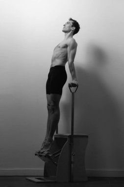 Zayıf erkek balerin pilates ekipmanlarıyla antrenman yapıyor. Zarif duruş, çekirdek gücü, vücut kontrolü. Yüksek kalite fotoğraf
