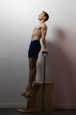 Zayıf erkek balerin pilates ekipmanlarıyla antrenman yapıyor. Zarif duruş, çekirdek gücü, vücut kontrolü. Yüksek kalite fotoğraf