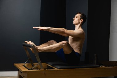 Zayıf erkek balerin pilates ekipmanlarıyla antrenman yapıyor. Zarif duruş, çekirdek gücü, vücut kontrolü. Yüksek kalite fotoğraf