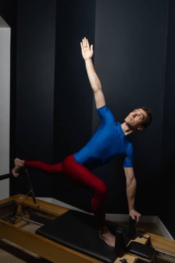 Zayıf erkek balerin pilates ekipmanlarıyla antrenman yapıyor. Zarif duruş, çekirdek gücü, vücut kontrolü. Yüksek kalite fotoğraf