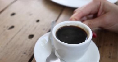 Şefkatli genç bir ev hanımı sıcak aromatik kahveyle bir fincanda şeker karıştırıyor. Genç ve çekici bir kadının elinin yakın planında doğal kahve aromalı bir bardakta şeker karıştırıyor. Taze kokulu. Yüksek kalite 4k görüntü