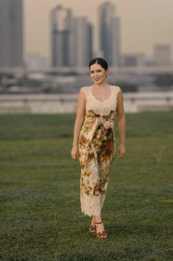 Güzel Doğu Avrupalı ya da beyaz bir kadın çiçekli kum renkli bir elbise içinde yüksek binalar ve şehir atmosferiyle modern bir şehrin siluetine poz veriyor. Şık ve zarif. Yüksek kalite fotoğraf