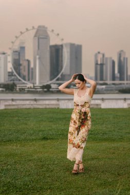 Güzel Doğu Avrupalı ya da beyaz bir kadın çiçekli kum renkli bir elbise içinde yüksek binalar ve şehir atmosferiyle modern bir şehrin siluetine poz veriyor. Şık ve zarif. Yüksek kalite fotoğraf