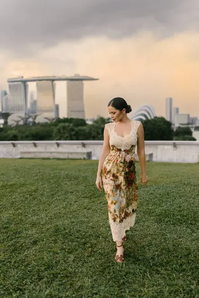 Marina Bay Sands Singapur siluetine karşı poz veren, çiçekli kum rengi bir elbise giymiş güzel Doğu Avrupalı ya da Kafkas bir kadın modern mimari ve şehir atmosferiyle. Yüksek kalite fotoğraf