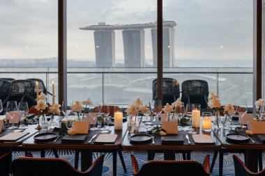 Marina Bay Sands ve Singapur ufuk çizgisini birinci elden gören şık bir yemek düzeni. Rafine sofra takımı ile lüks restoran ortamı, sofistike bir şehir deneyimi sunuyor..