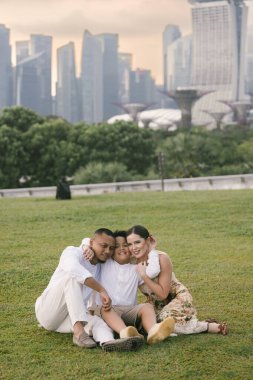 Uzun, modern gökdelenlerin önünde poz veren mutlu uluslararası aile. Asyalı baba, Doğu Avrupalı anne ve 7 yaşındaki melez çocukları şehirde birlikte vakit geçiriyorlar. Yüksek kalite fotoğraf