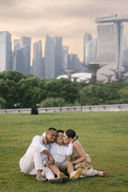 Uzun, modern gökdelenlerin önünde poz veren mutlu uluslararası aile. Asyalı baba, Doğu Avrupalı anne ve 7 yaşındaki melez çocukları şehirde birlikte vakit geçiriyorlar. Yüksek kalite fotoğraf