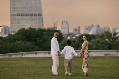 Uzun, modern gökdelenlerin önünde poz veren mutlu uluslararası aile. Asyalı baba, Doğu Avrupalı anne ve 7 yaşındaki melez çocukları şehirde birlikte vakit geçiriyorlar. Yüksek kalite fotoğraf
