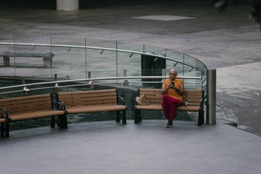 Singapur, 28 Mayıs 2025: Ulusal kostümlü Asyalı bir adam, Singapur 'un çok kültürlü kültürel mirasını temsil eden bir bankta huzur içinde oturuyor. Yüksek kalite fotoğraf