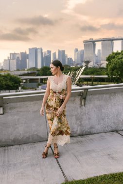Marina Bay Sands 'e ve modern Singapur siluetine karşı emin bir şekilde poz veren şık kıyafetli, koyu renk saçlı güzel bir genç kadın. Güzellik, kendine güven, zarafet ve şehir cazibesi. Yüksek kalite fotoğraf