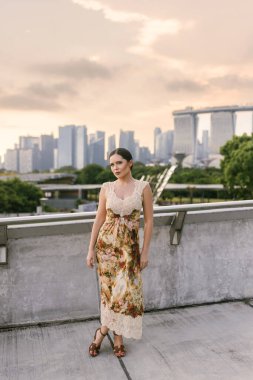 Marina Bay Sands 'e ve modern Singapur siluetine karşı emin bir şekilde poz veren şık kıyafetli, koyu renk saçlı güzel bir genç kadın. Güzellik, kendine güven, zarafet ve şehir cazibesi. Yüksek kalite fotoğraf