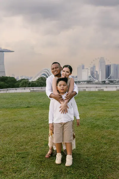 Uzun, modern gökdelenlerin önünde poz veren mutlu uluslararası aile. Asyalı baba, Doğu Avrupalı anne ve 7 yaşındaki melez çocukları şehirde birlikte vakit geçiriyorlar. Yüksek kalite fotoğraf