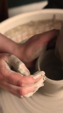 Zanaatkar bir stüdyoda çömlek çarkında çamurla çalışan ellerin yakın çekimi. Yaratıcı hobi, aktif seramik sanat ve özenli el işçiliği. Yüksek kalite 4k görüntü