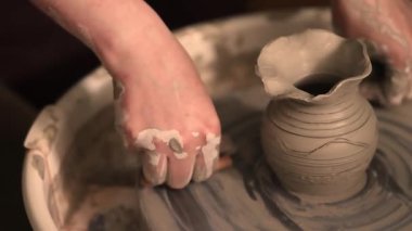 Zanaatkar bir stüdyoda çömlek çarkında çamurla çalışan ellerin yakın çekimi. Yaratıcı hobi, aktif seramik sanat ve özenli el işçiliği. Yüksek kalite 4k görüntü
