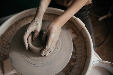 Çamurla kaplı eller yaratıcı bir çömlek atölyesinde dönen çarkın üzerinde seramik bir parça. Dokunsal dokuları ve toprak tonlarıyla sanatsal el yapımı bir süreç. Hobi ve zanaat ele geçirildi.