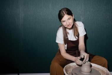  Sıcak çömlek atölyesinde kil yuvarlarken önlüklü gülümseyen kadın çömlekçi. Neşeli sanatsal hobi. Yüksek kalite 4k görüntü