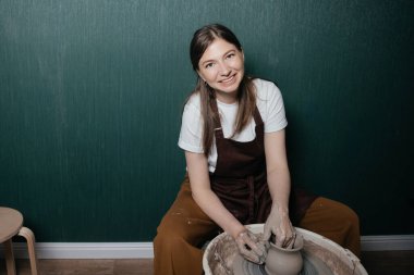  Sıcak çömlek atölyesinde kil yuvarlarken önlüklü gülümseyen kadın çömlekçi. Neşeli sanatsal hobi. Yüksek kalite 4k görüntü