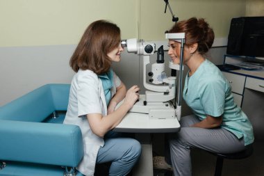 Oftalmolojist, klinikteki hastaların gözlerini profesyonel teşhis cihazıyla muayene ediyor. Göz testi yapılıyor. Klinik ortamlarda vizyon taraması ve sağlık kontrolü.