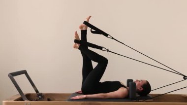 Siyah dar spor giysili zayıf esmer kadın Pilates reformatında çalışıyor. Parlak fitness stüdyosundaki pilates seansı sırasında kasları esnetme ve yumuşatma. Yüksek kalite 4k görüntü