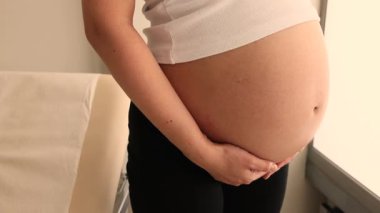 Beyaz kolsuz tişörtlü beyaz bir kadının hamile karnını kapatın. Yüksek kalite 4k görüntü