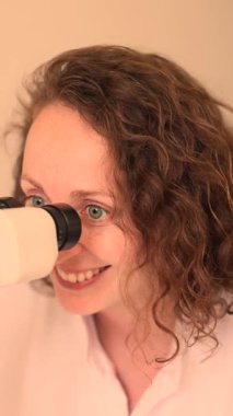 Klinikteki tıbbi mikroskoba bakarken gülümseyen kızıl saçlı kadın doktor. Yüksek kalite 4k görüntü