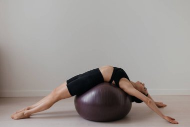 Siyah pilates topu üzerinde egzersiz yapan ince, beyaz tenli, esmer bir kadın. Yüksek kalite fotoğraf