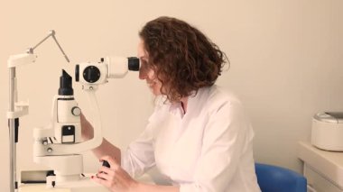 Klinikte profesyonel göz teçhizatı kullanarak gülümseyen kızıl saçlı kadın doktor. Yüksek kalite 4k görüntü