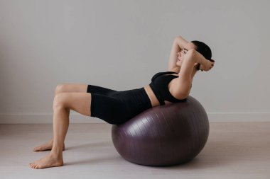 Siyah pilates topu üzerinde egzersiz yapan ince, beyaz tenli, esmer bir kadın. Yüksek kalite fotoğraf