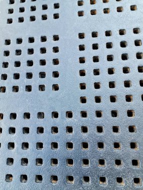 Gri metal duvarın dikey bir görüntüsü ve deseninde bir sürü kare deliği var..