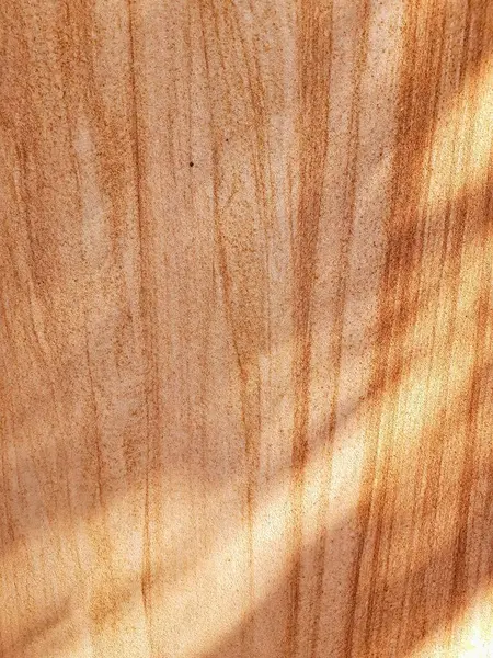 Kahverengi, altın ve beyaz renklerle desenli kumtaşının yakın çekimi. Ağaçtaki yapraklardan gölgeler görebilirsin..