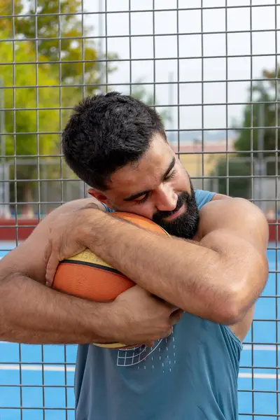Şehirdeki basketbol sahasında elinde basketbol topu tutan beyaz bir genç.