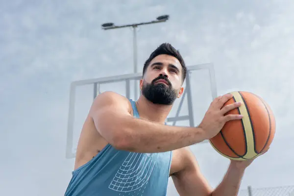 Mavi tişörtlü çocuk güneşli bir günde dışarıda basketbol oynuyor.