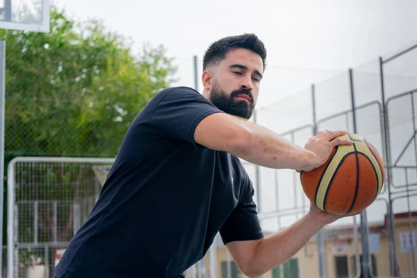 Siyah tişörtlü çocuk güneşli bir günde dışarıda basketbol oynuyor.