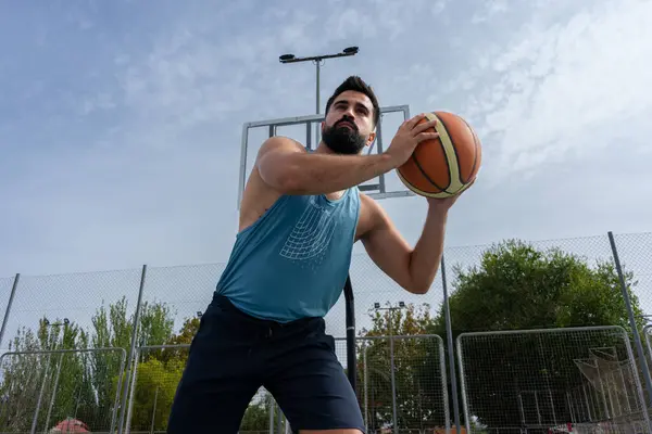 Mavi tişörtlü çocuk güneşli bir günde dışarıda basketbol oynuyor.