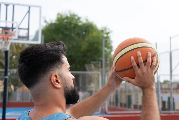 Mavi tişörtlü çocuk güneşli bir günde dışarıda basketbol oynuyor.