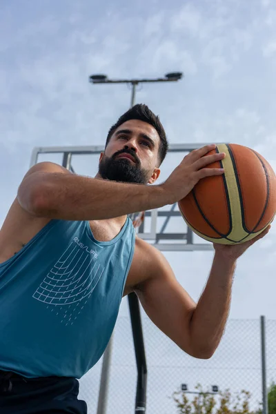 Mavi tişörtlü çocuk güneşli bir günde dışarıda basketbol oynuyor.